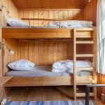 Bunk bed in a wood-paneled room with window and wall lamp.