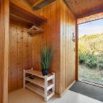 Entrance with wooden walls, shoe rack, and plant. Door opens to green outdoor view.