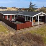 Red wooden house with terrace and garden. View of surrounding houses.
