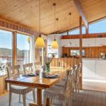 Dining room with wooden table, chairs, and kitchen area with white cabinets.
