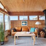 Living room with wood walls, sofa, stove, and large windows.