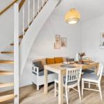 Dining area with table, chairs, and staircase. Wall shelf and pendant light visible.