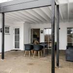 Terrace with table, chairs, and plants under wooden structure.