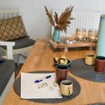 Wooden table with mugs, dice, and candles on placemats. Background: seating and dried plants.