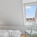 Bedroom with skylight, view of rooftops and blue sky. Wooden floor, bed, chair, and nightstand.