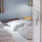 Schlafzimmer mit Bett, Kissen und Nachttisch. Vorhang und Lampe sind sichtbar.