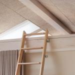 Holzleiter führt zu einer Dachbodenwohnung mit Dachschräge und Fenster.
