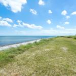 Weiterer Blick auf den Strand mit Grasland und blauem Himmel mit weißen Wolken.
