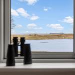 Durch das Fenster blickt man auf einen Fluss und eine Schiffsluke im Hintergrund.