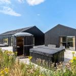 Zwei schwarze Holzhäuser mit Sauna und Whirlpool auf einer Terrasse inmitten von Blumen.