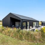 Moderne schwarze Hütte mit Terrasse, Grill und Außensitzgelegenheit in ländlicher Umgebung.