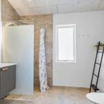 Badezimmer mit Dusche, Waschbecken und Toilette. Fenster, Spiegel und Holzstufen.