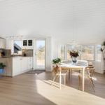 Kitchen and dining area with wooden floor, white walls, and large windows.