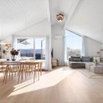 Living and dining area with wooden floor, large sofa, and dining set under high ceiling.