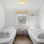 Two beds with bedding, window and stool in the room.