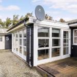 House with glass front, wooden terrace, and satellite dish. Rear yard with gravel and outbuilding.