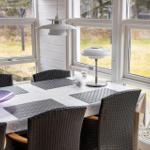 Dining table with chairs and tablecloth by large windows.