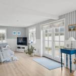 Living room with sofa, TV, and windows. Striped wallpaper and wooden floor.