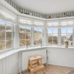 Room with bay windows, white walls, and wooden floor. Plants and decor are on the windowsill.