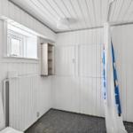 Bathroom with shower, toilet, and window. White walls and floor tiles.