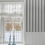 Window with sheer curtains, two lit candles, and striped wall.