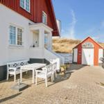 House with white seating area and red extension. Plants and pavilion in background.