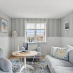 Living room with striped walls, sofa and chair. Windows with roller blinds and rug.