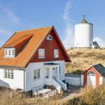A red house with white lower section and orange roof. Behind it stands a white windmill structure.