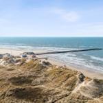Beach with dunes, boathouses, and pier. View of the sea.