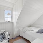 Bedroom with sloped ceiling, bed and armchair. Windows with view outside.