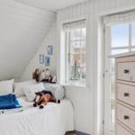 Bedroom with white bed, wooden floor, and window with sailboat model.