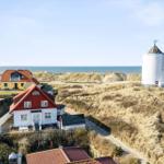 House with red roof, white facade, and view of the sea and a windmill.