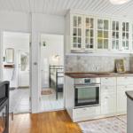Kitchen with white cabinets, stone backsplash, and wooden floor. Bedroom visible in background.