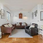 Living room with brown leather sofas, wooden floor, and white walls with pictures.
