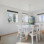 Dining room with white tablecloth and chairs, wooden floor, and windows with view outside.