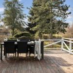 Deck with dining table and chairs, surrounded by trees and greenery.