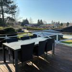 Deck with table and chairs, view of houses and trees.