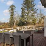 Deck with table, chairs, and lounge chair. View of trees and holiday home.