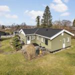 Green house with garden and grill area under blue sky.