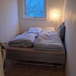 Schlafzimmer mit Bett, Fenster und Wandlampe.