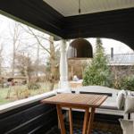 Veranda mit Tisch, Sitzbank und Hängelampe. Blick auf Garten und Bäume.