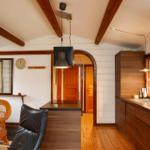 Küche mit Holzschrank, Spüle und Mikrowelle. Im Hintergrund Sitzgelegenheit und Türen.
