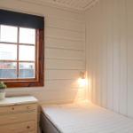 Ein Schlafzimmer mit weißer Wandverkleidung, einem Bett, einem Schrank und einem Fenster.