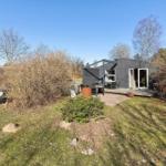 Moderne Hütte mit Terrasse, Garten und Sitzbank. Umgeben von Bäumen und Sträuchern.