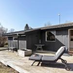 Holzterrasse mit Liegestuhl, Tisch und Grillbereich vor einem Haus mit offener Tür.