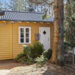 Gelbes Haus mit weißer Tür und Fenstern, umgeben von Bäumen und Sträuchern.