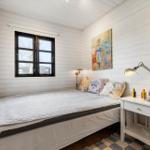 Schlafzimmer mit Bett, Nachttisch und Fenster. Wände sind weiß verputzt.