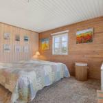 Schlafzimmer mit Holzwand, Bett, Fenster und Kunstwerken.