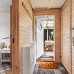 Schlafzimmer mit Bett und Wandbild. Flur führt zur Terrasse. Holzwände und Tür.