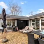 Terrasse mit Liegestühlen, Tisch und Sonnenschirm. Haus mit Glasfronten und dunklem Holz.
